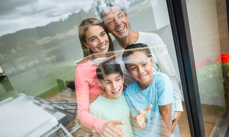 A family of four smiles while looking out of a large window.